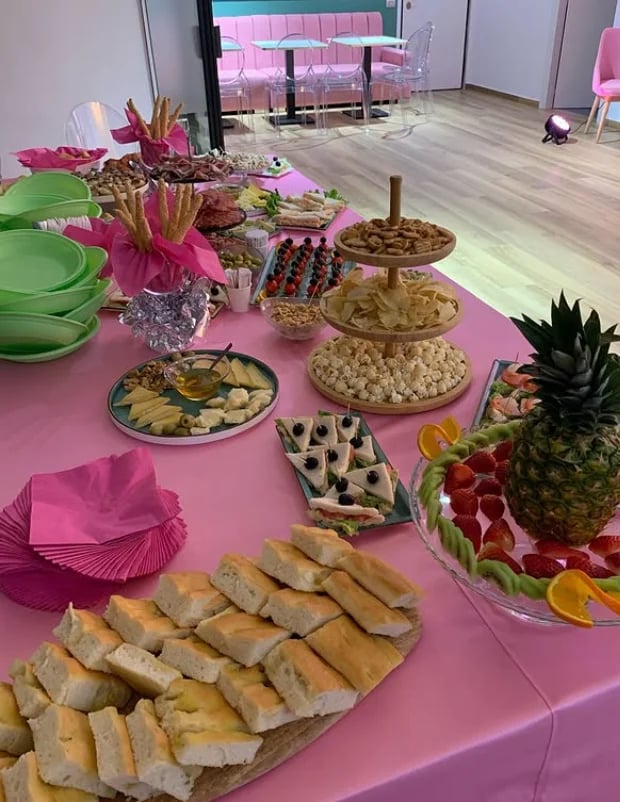 Pink buffet table with assorted appetizers, pastries, fresh fruit, and tiered cake stand at an event venue