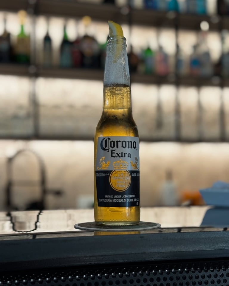Open Corona Extra beer bottle sitting on a dark surface with industrial warehouse background