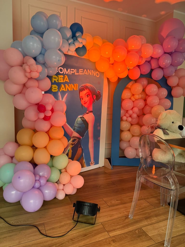 Colorful balloon garland arch in pastel colors framing a blue poster for an 8th birthday celebration party setup