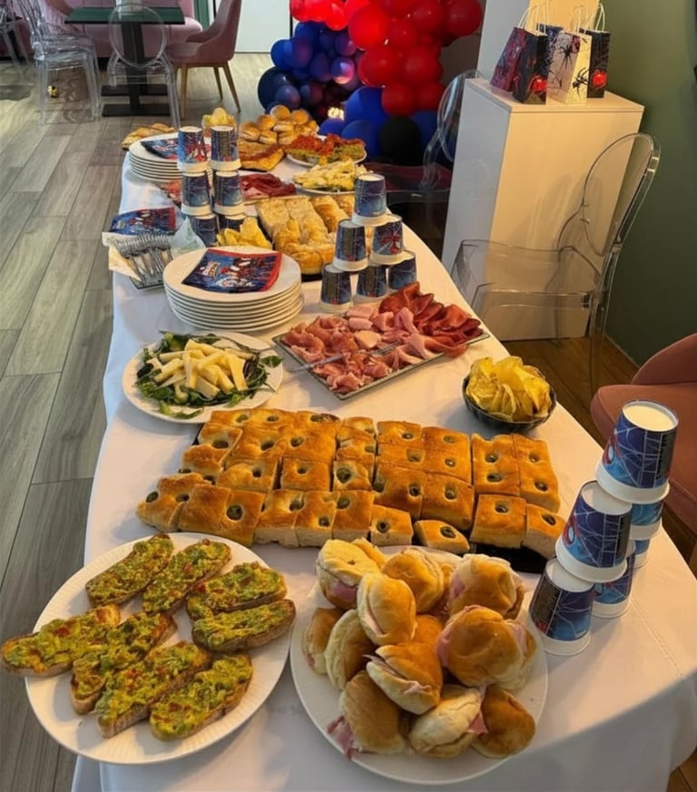 Party spread with charcuterie, bread, rolls, appetizers, and desserts on white tables with red and blue balloon decorations in background