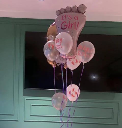Pink and white baby shower balloons with Its a Girl message displayed against a mint green wall and dark window