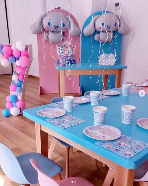 Childrens party setup with pink and blue balloon garlands, decorative cloud cutouts, table with character-themed plates and cups