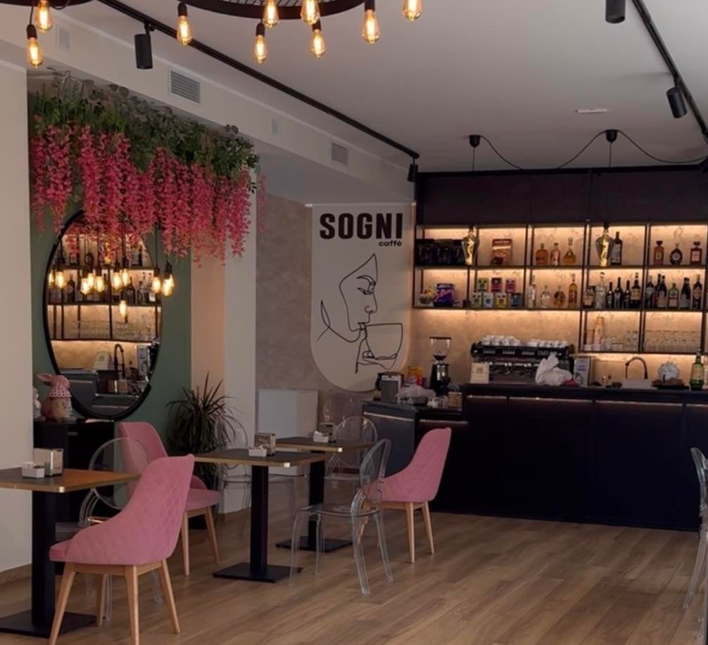 Modern salon interior with pink chairs, black counter, decorative hanging flowers, and illuminated product shelves